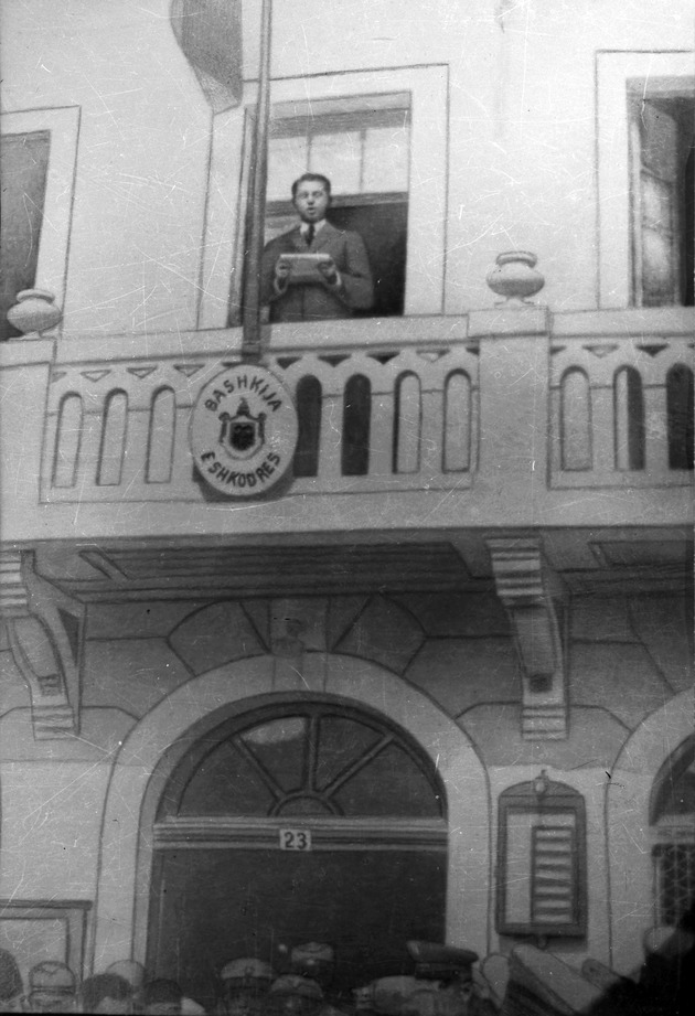 Fotografia e manipuluar e Enver Hoxhës tek mbante fjalim e publikuar në librin _Gjurmë të historisë kombëtare në Fototekën e Shkodrës_ në 1982.